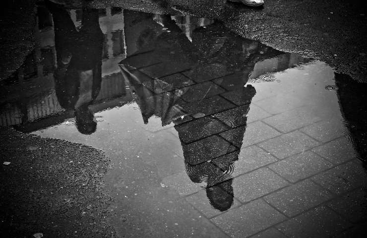 Pozzanghera che riflette persone con ombrelli